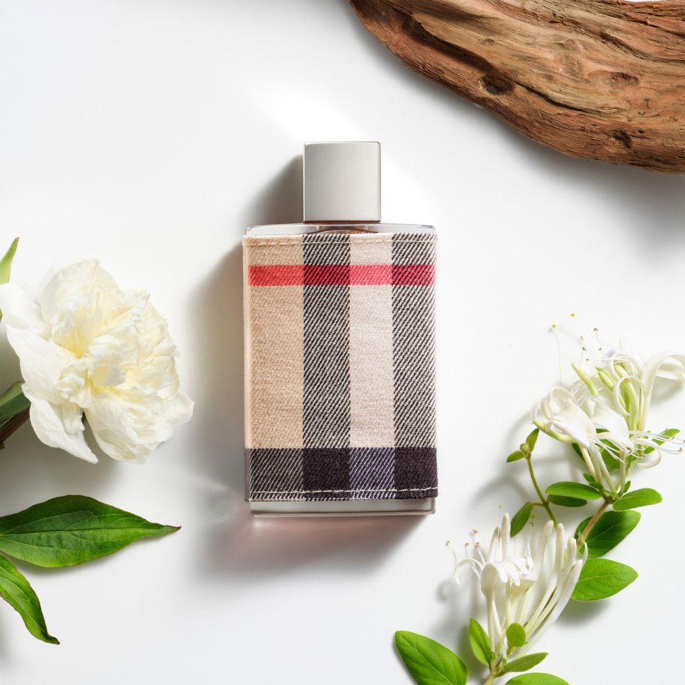 Parfümflakon mit kariertem Stoffbezug. Blüten und Holzstück auf weißem Hintergrund.