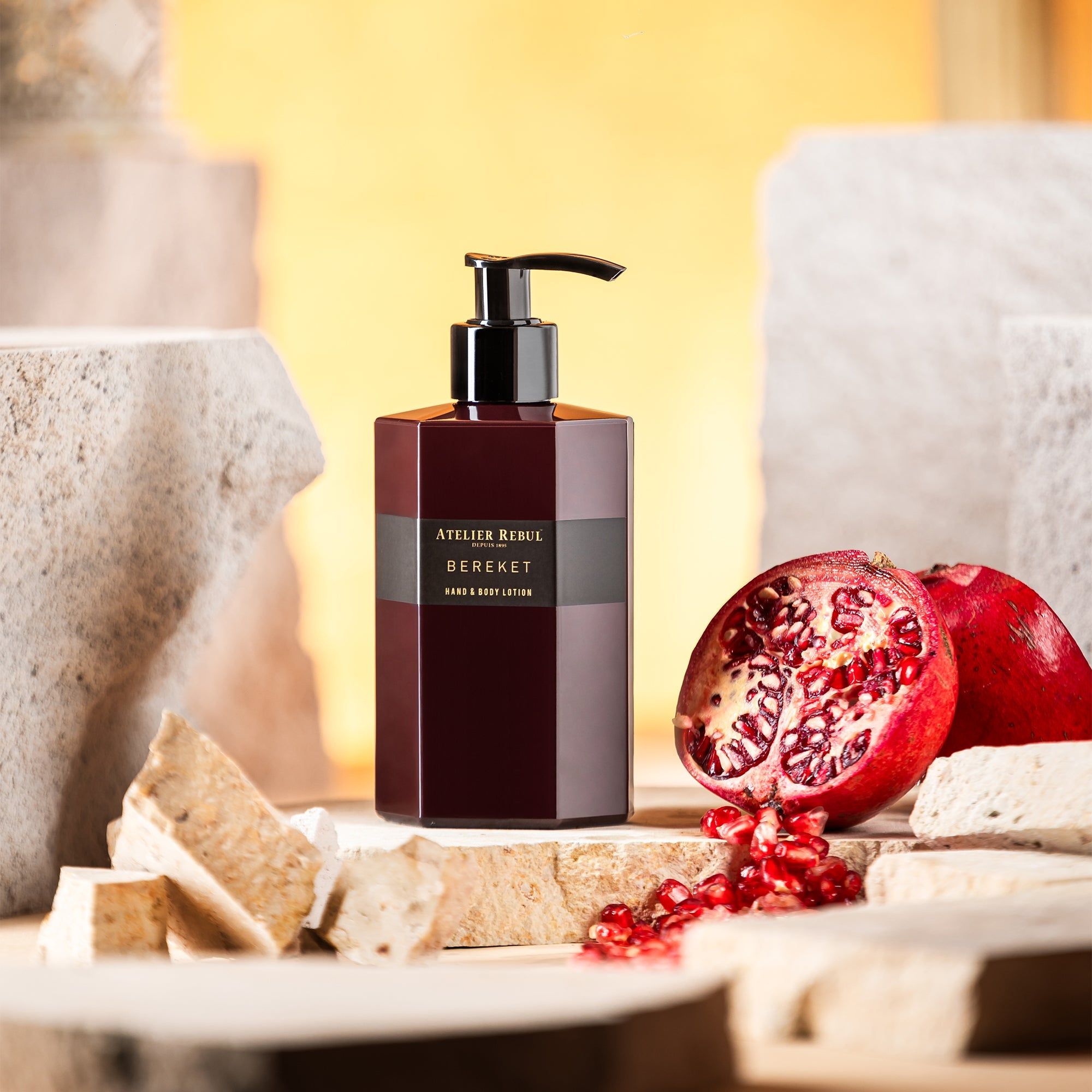 Bordeauxfarbene Lotionflasche mit schwarzem Pumpkopf. Aufschrift: Atelier Rebul Bereket Hand & Body Lotion. Granatapfel daneben.
