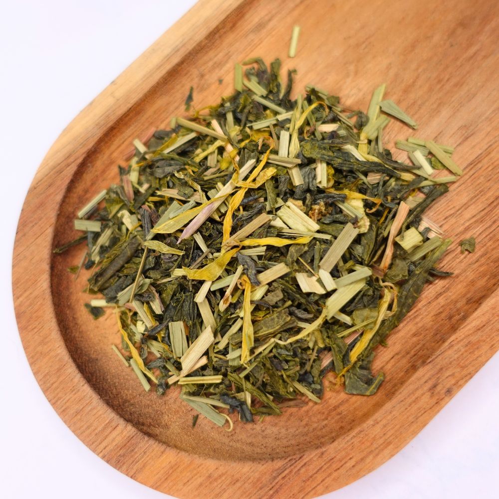 Grüner Tee mit Zitronengras in einer Holzschale. Die Mischung enthält grüne Teeblätter und gelbes Zitronengras.