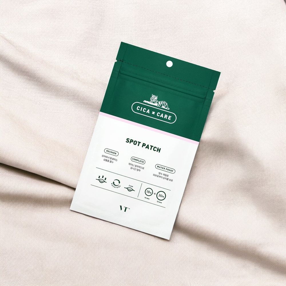 Grüne Verpackung mit weißem Text auf beigem Stoff. Auf der Verpackung steht "CICA x CARE SPOT PATCH" und das Logo.