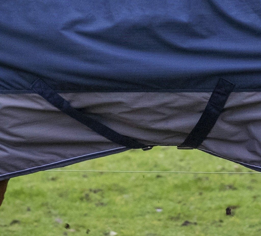 Nahaufnahme der Unterseite einer blauen und grauen Pferdedecke. Riemen und Schnallen sichtbar.