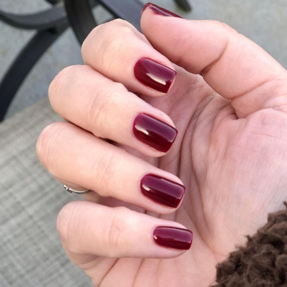 Hand mit lackierten Nägeln in dunklem Rot. Quadratische Form, glänzendes Finish. Ring am Finger.