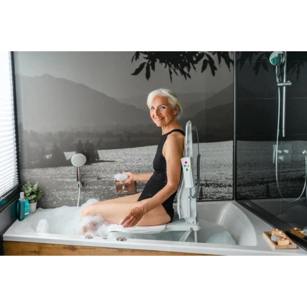 Frau sitzt in Badewanne mit Badewannenlift. Bedienfeld am Lift. Hintergrund: Landschaft.