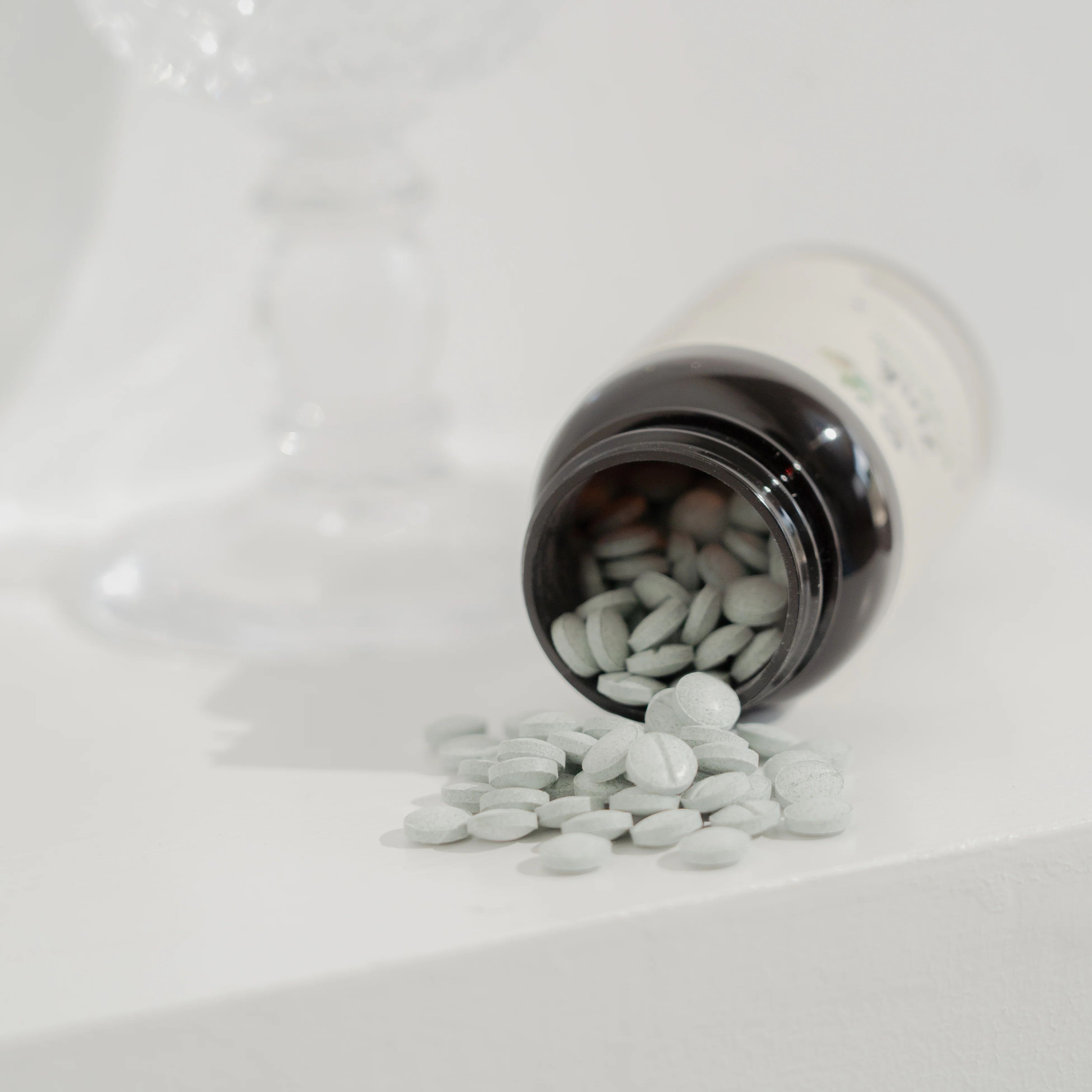 Braune Flasche, Tabletten liegen daneben. Tabletten sind hellgrün. Flasche geöffnet, Tabletten fallen heraus.
