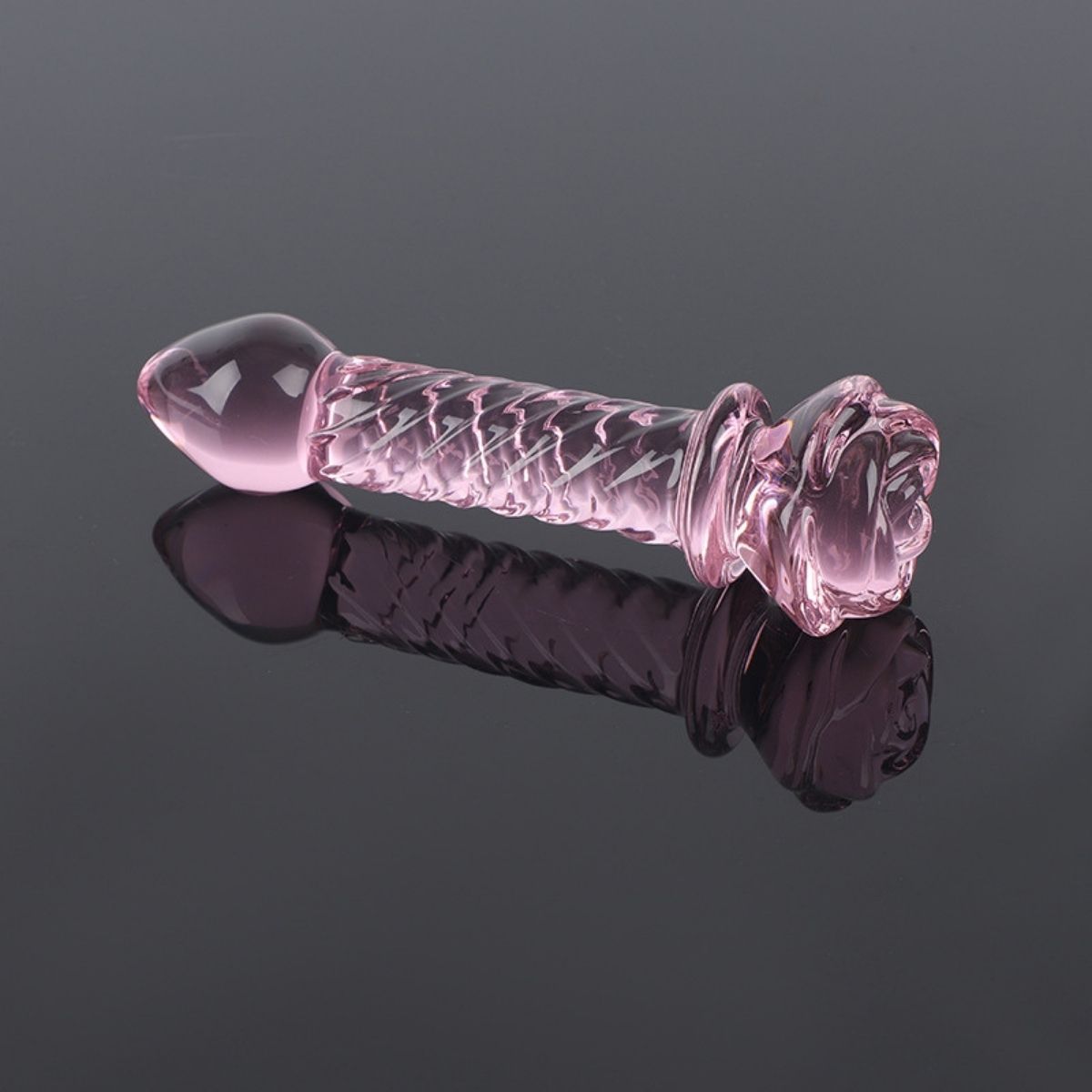 Rosa Glasstab mit geriffelter Oberfläche und blütenförmigem Griff. Auf glänzendem, dunklem Untergrund.