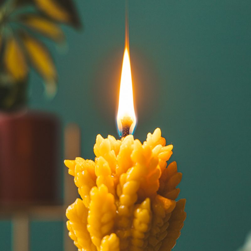 Brennende gelbe Wachskerze in Form eines Weizenbündels. Flamme sichtbar.