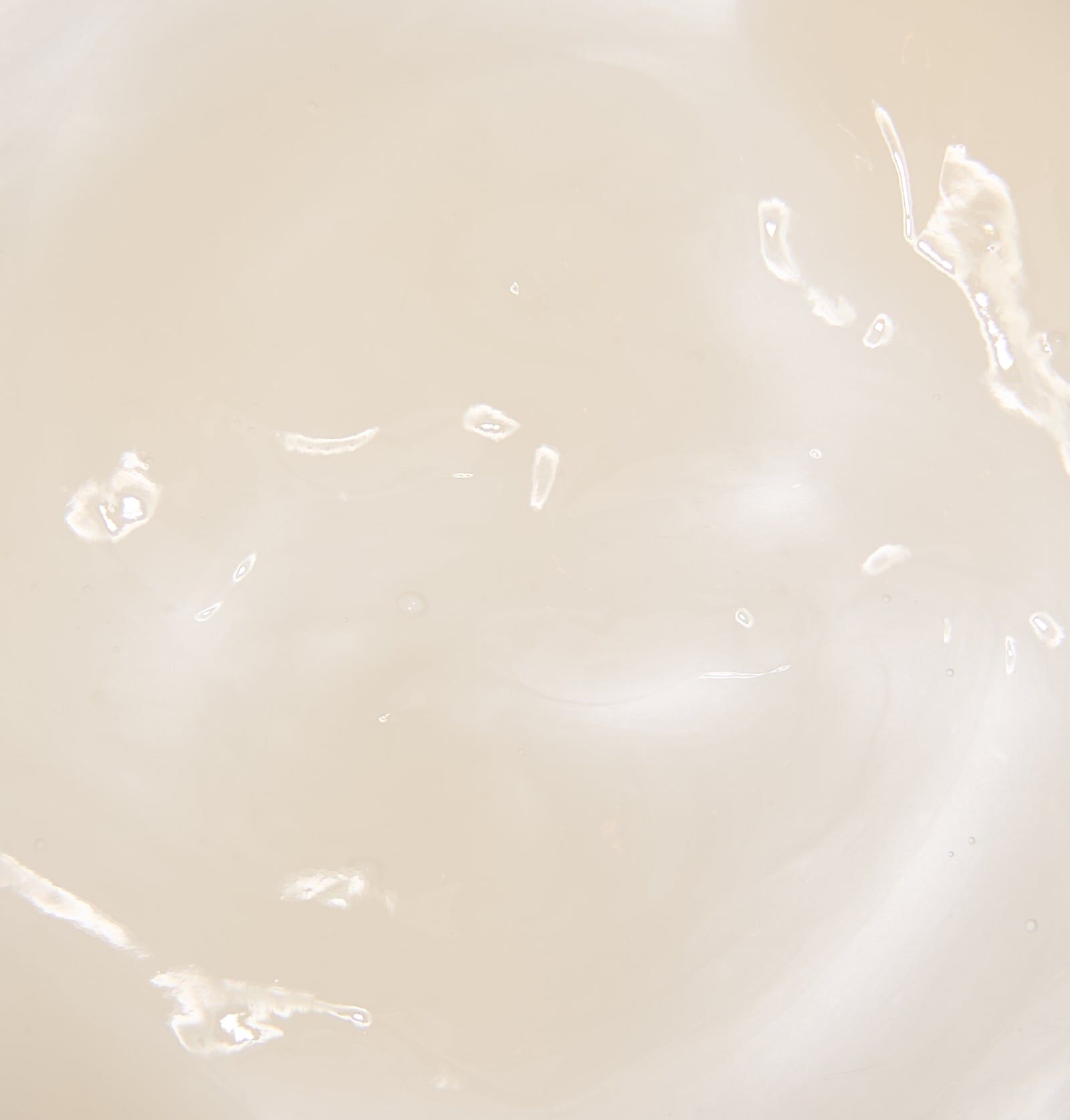 Nahaufnahme einer cremigen, hellen Flüssigkeit. Einige Tropfen und Wirbel sind sichtbar. Textur.