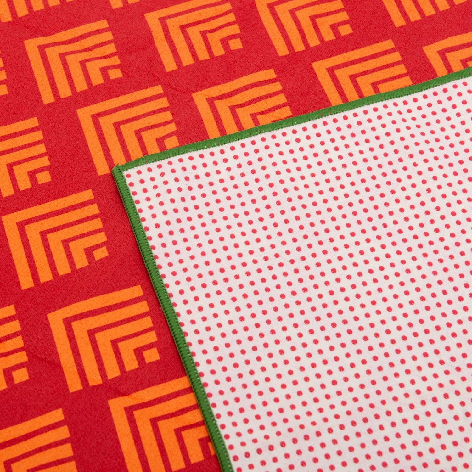 Yoga-Handtuch, rot-gelb. Geometrische Muster, grüne Ränder und weiße Rückseite mit roten Punkten.