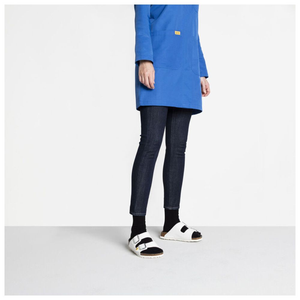 Person trägt weiße Birkenstock-Sandalen. Blaue Jacke und dunkle Hose. Schwarze Socken.