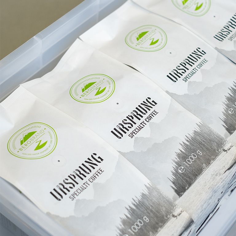 Mehrere Kaffeebohnen-Verpackungen. Weiß, mit Logo und Text. In einer transparenten Box.