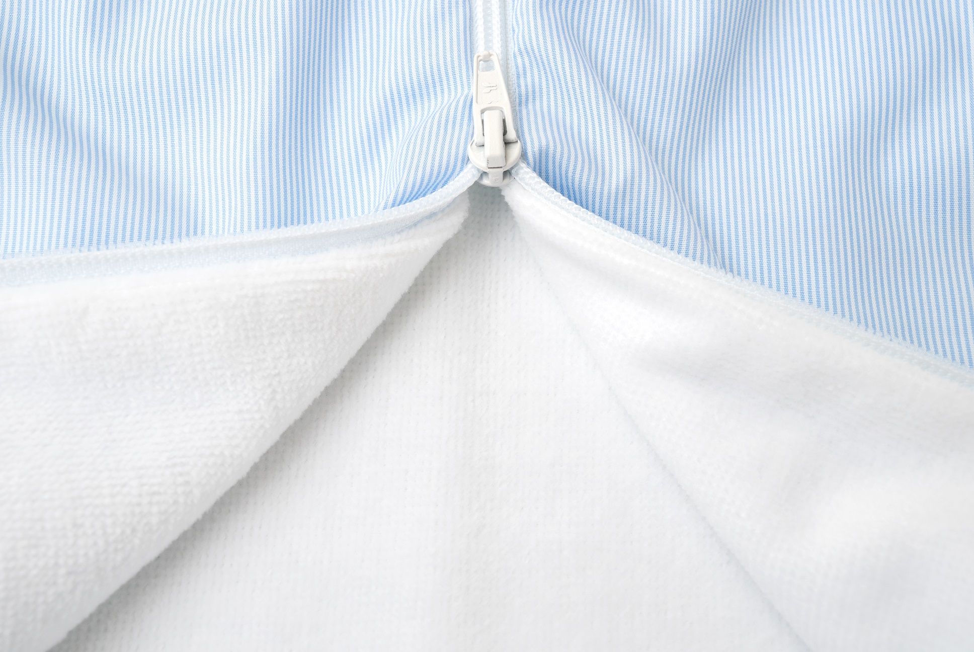 Nahaufnahme Reißverschluss eines Frottierschlafsacks. Hellblau gestreiftes Außenmaterial, weißes Innenfutter.