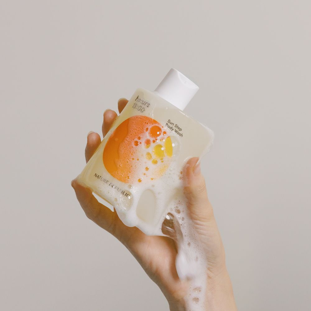 Hand hält eine Flasche mit Schaum. Flasche: ho:urs, Sun Step Body Wash. Schaum fließt aus der Flasche.