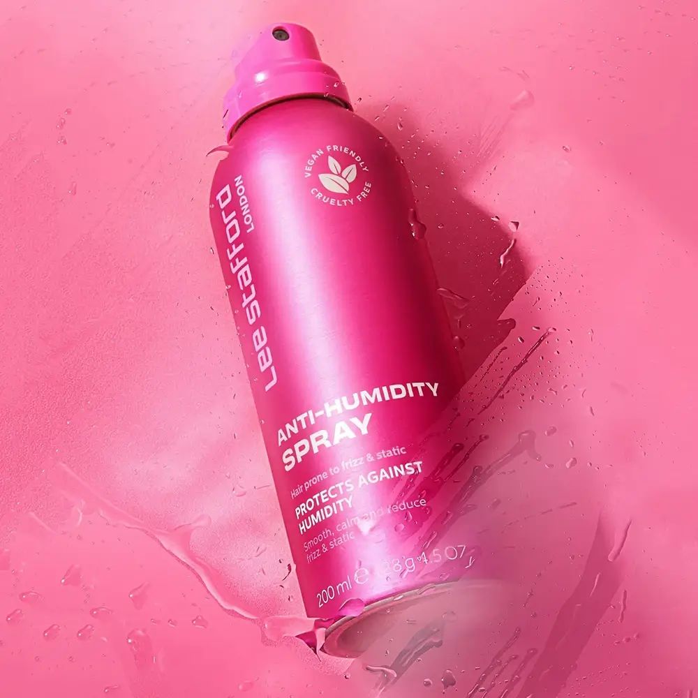 Rosa Sprühflasche, Lee Stafford Anti-Humidity Spray. Vegan- und tierversuchsfrei. Auf rosa Untergrund mit Wasser.