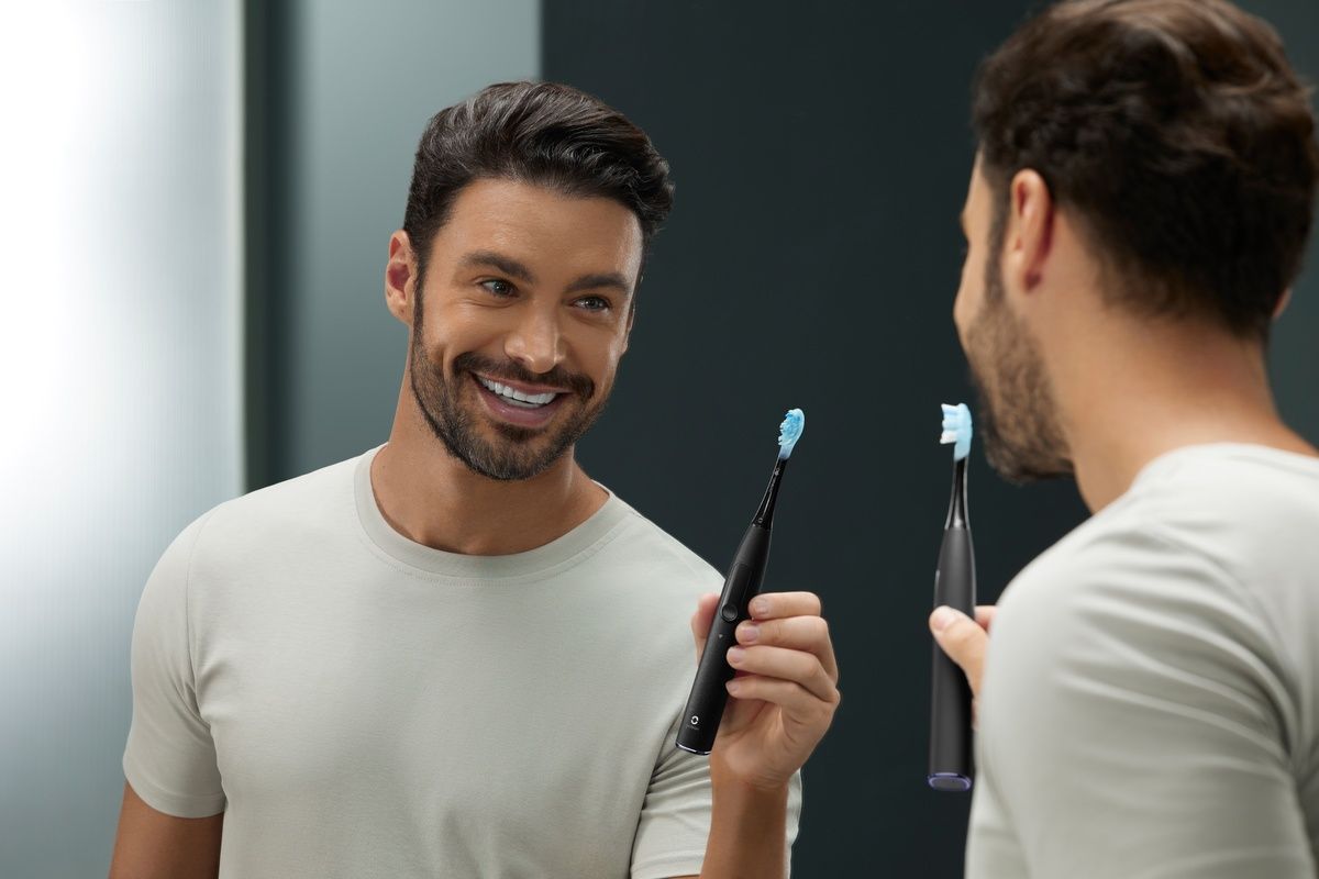 Mann im Badezimmer, der sich im Spiegel mit einer elektrischen Zahnbürste die Zähne putzt. Spiegelbild.