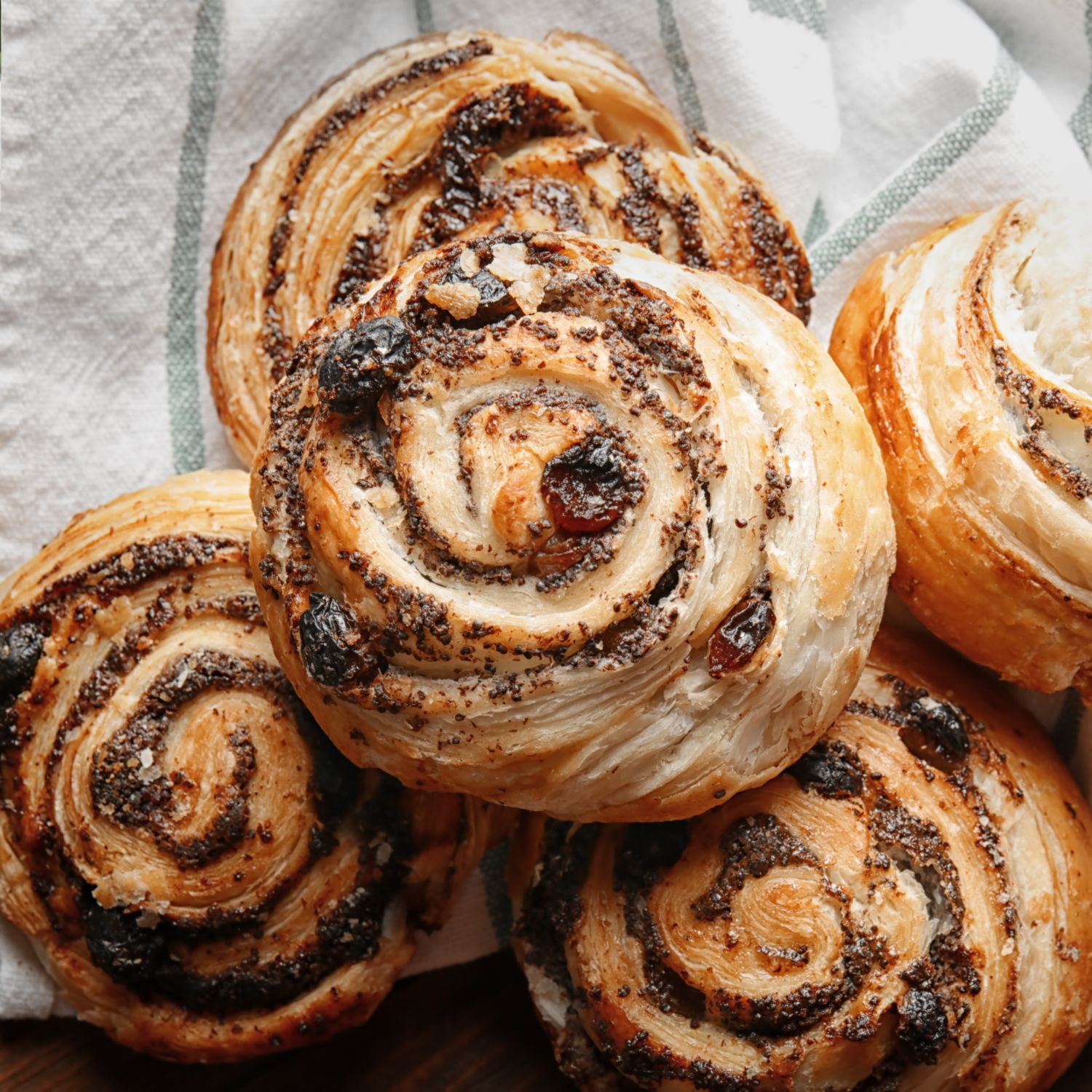 Gebäck mit Mohnfüllung. Mehrere Schnecken auf einem weißen Tuch. Sichtbare Mohnfüllung und Rosinen.