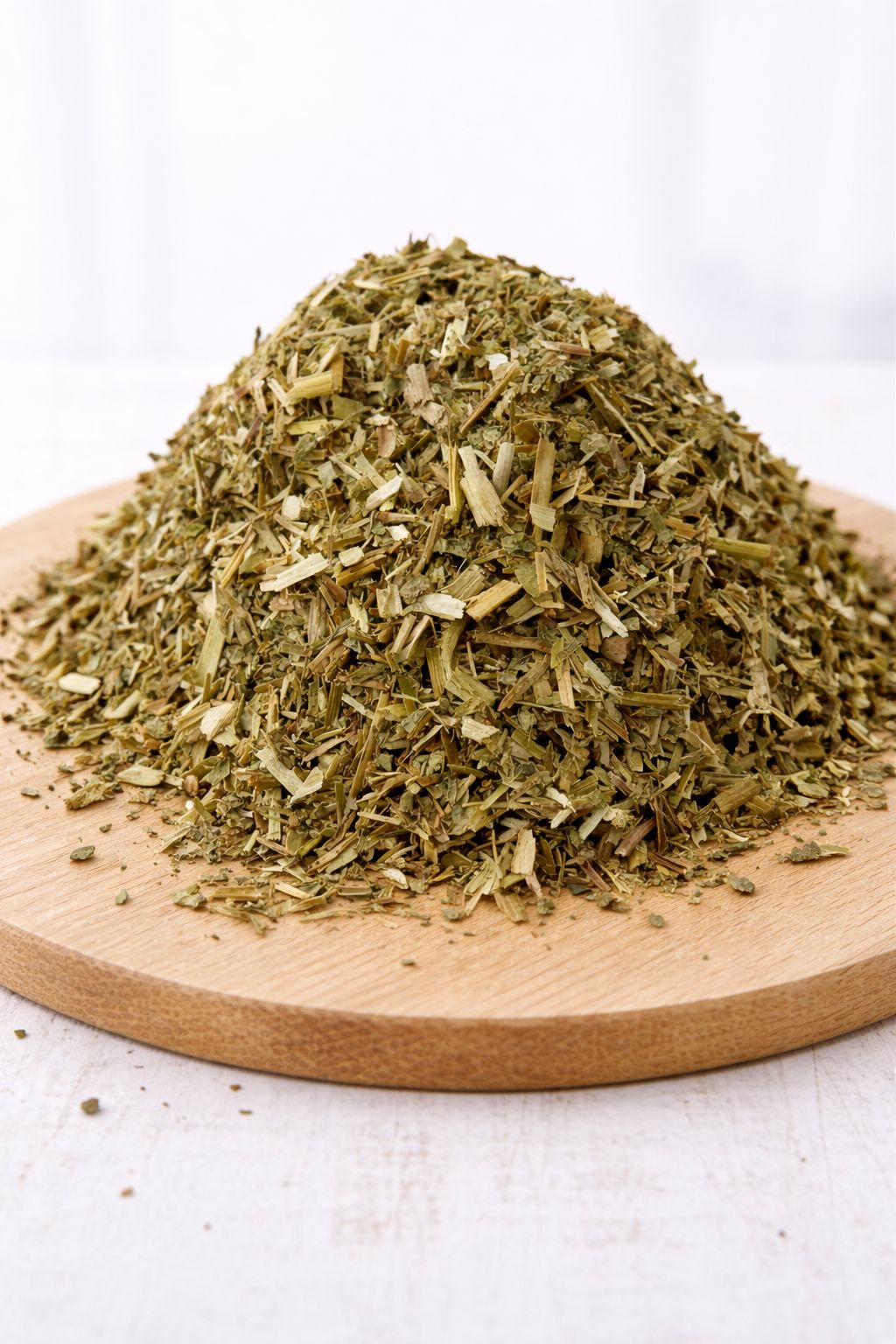 Haufen getrockneter, grüner Kräuter auf einem Holzbrett. Die Kräuter sind grob geschnitten.