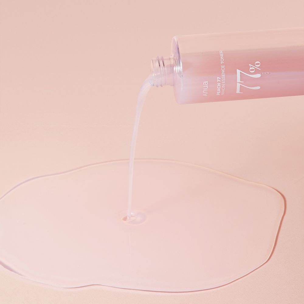 ANUA Peach 77% Niacin Essence Toner wird aus einer Flasche auf eine Oberfläche gegossen.