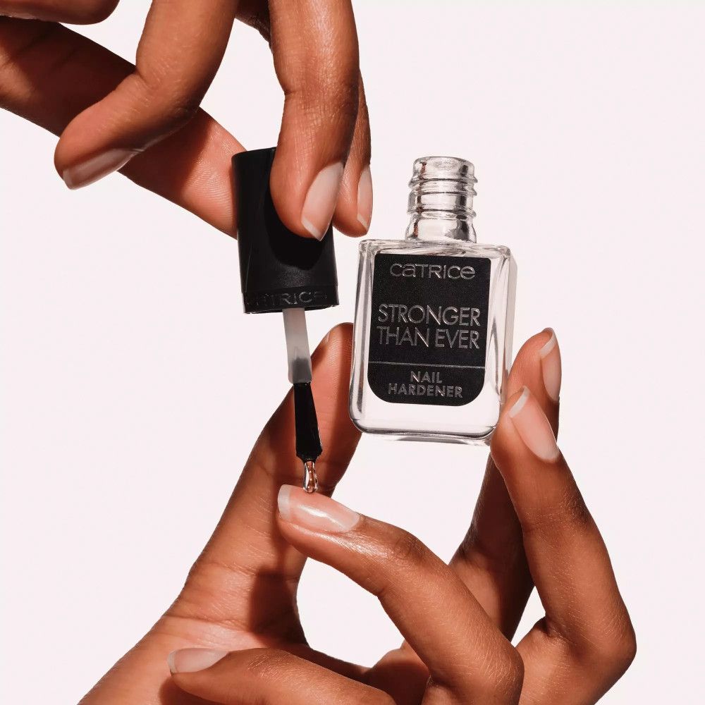 Hände halten eine Nagelhärter-Flasche mit geöffnetem Deckel und Pinsel. Aufschrift: Catrice, Stronger Than Ever, Nail Hardener.
