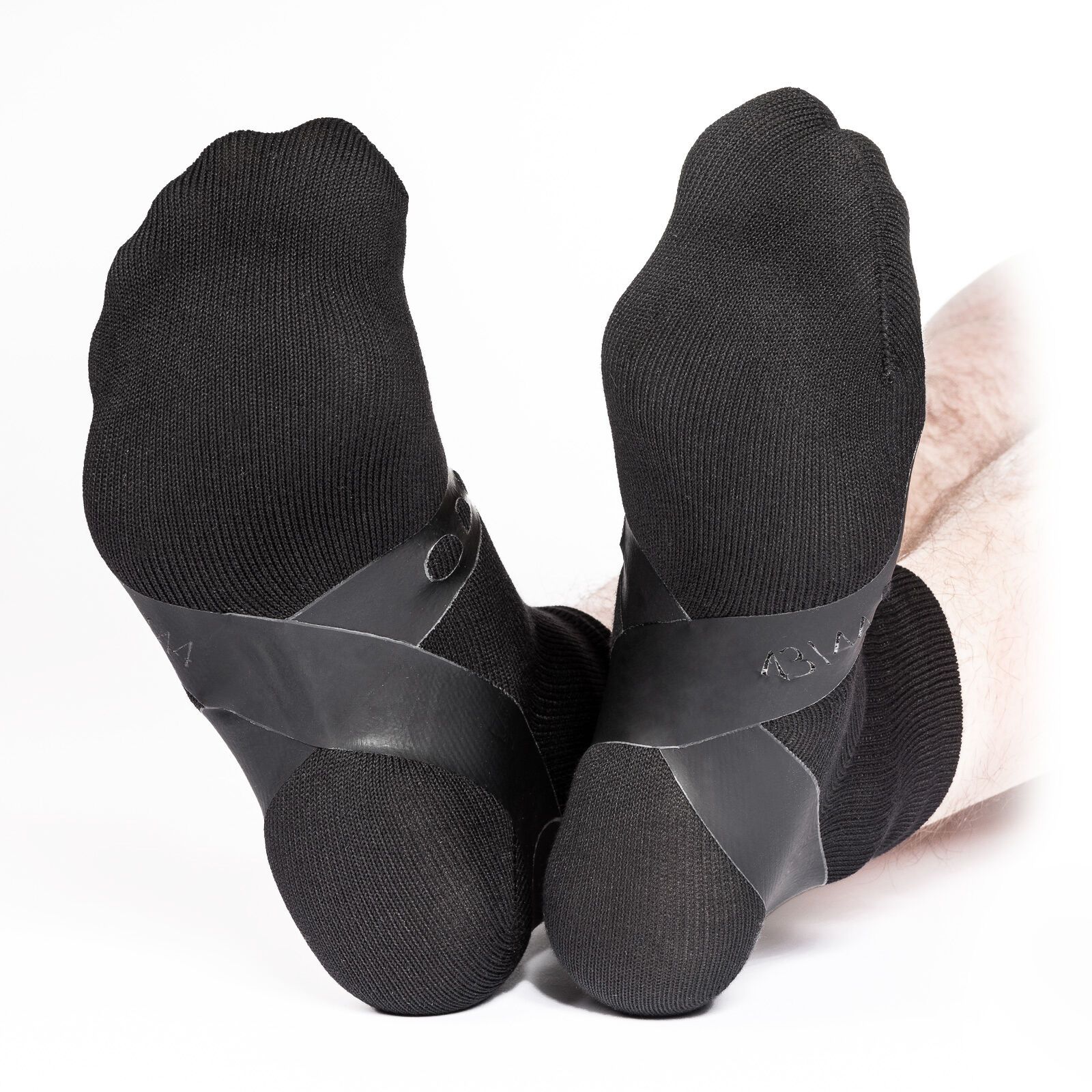 Zwei schwarze Socken mit integrierten, schwarzen, stabilisierenden Elementen. Unteransicht der Füße.