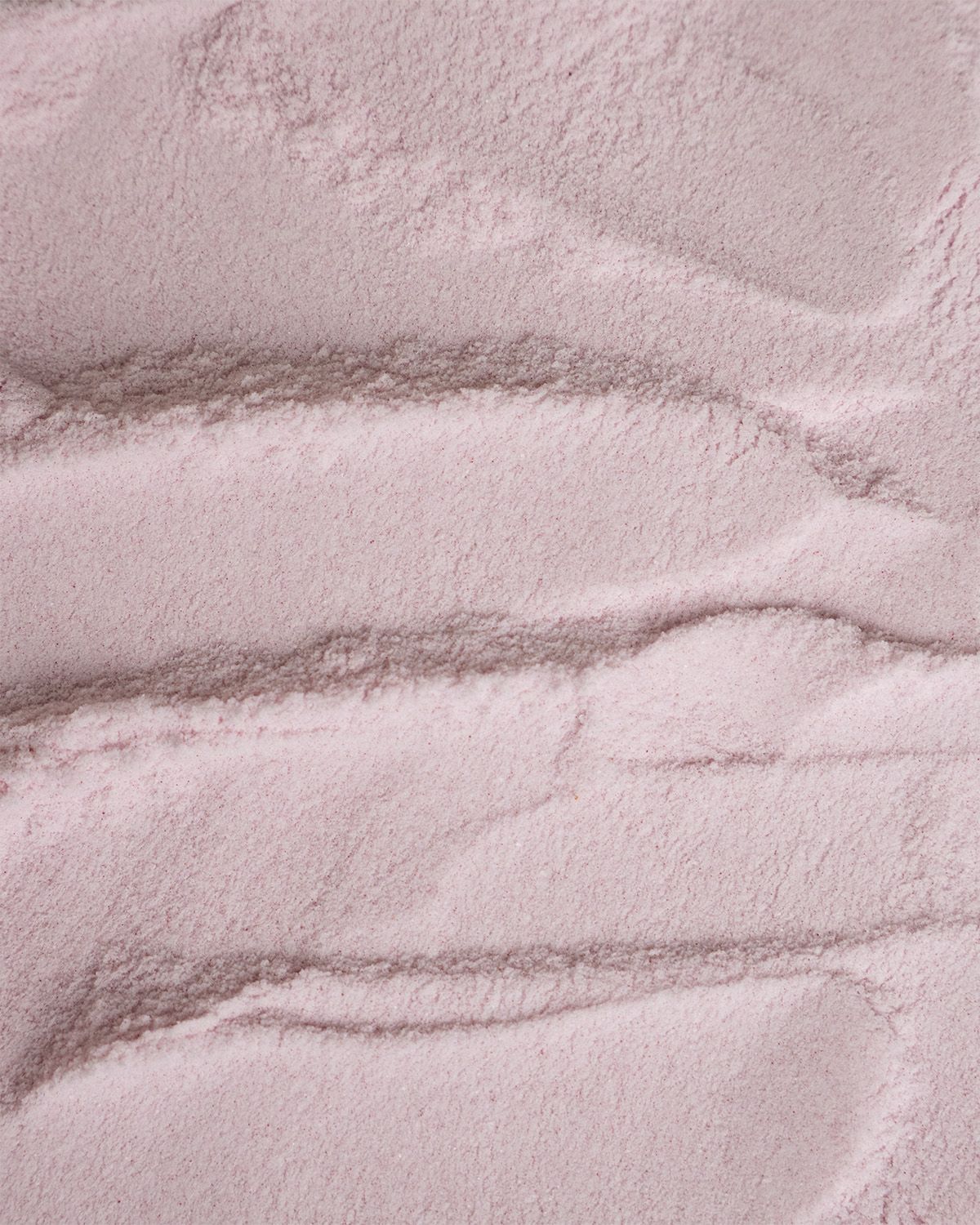 Nahaufnahme von rosa Pulver mit wellenförmiger Textur. Helle Beleuchtung.