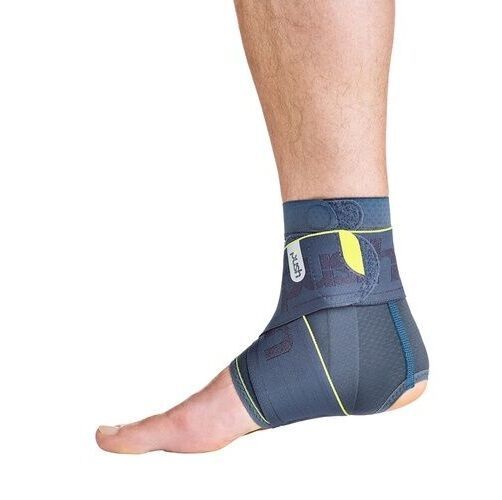 Knöchelbandage am Fuß. Grau-blaues Material mit gelben Akzenten. Klettverschluss und Logo sichtbar.