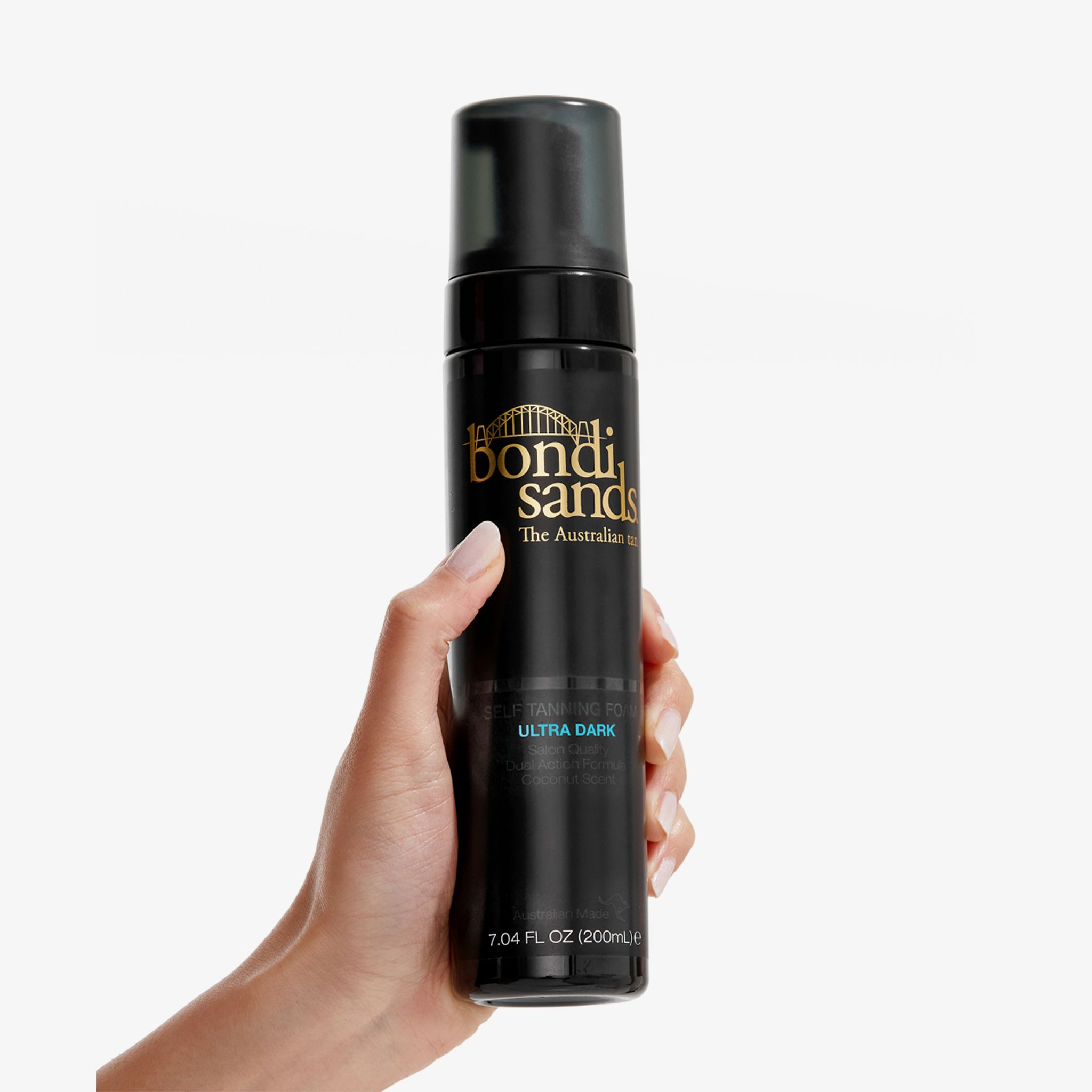 Hand hält eine schwarze Flasche mit schwarzem Sprühkopf. Aufschrift: Bondi Sands, Ultra Dark Selbstbräunungsschaum. 200ml.