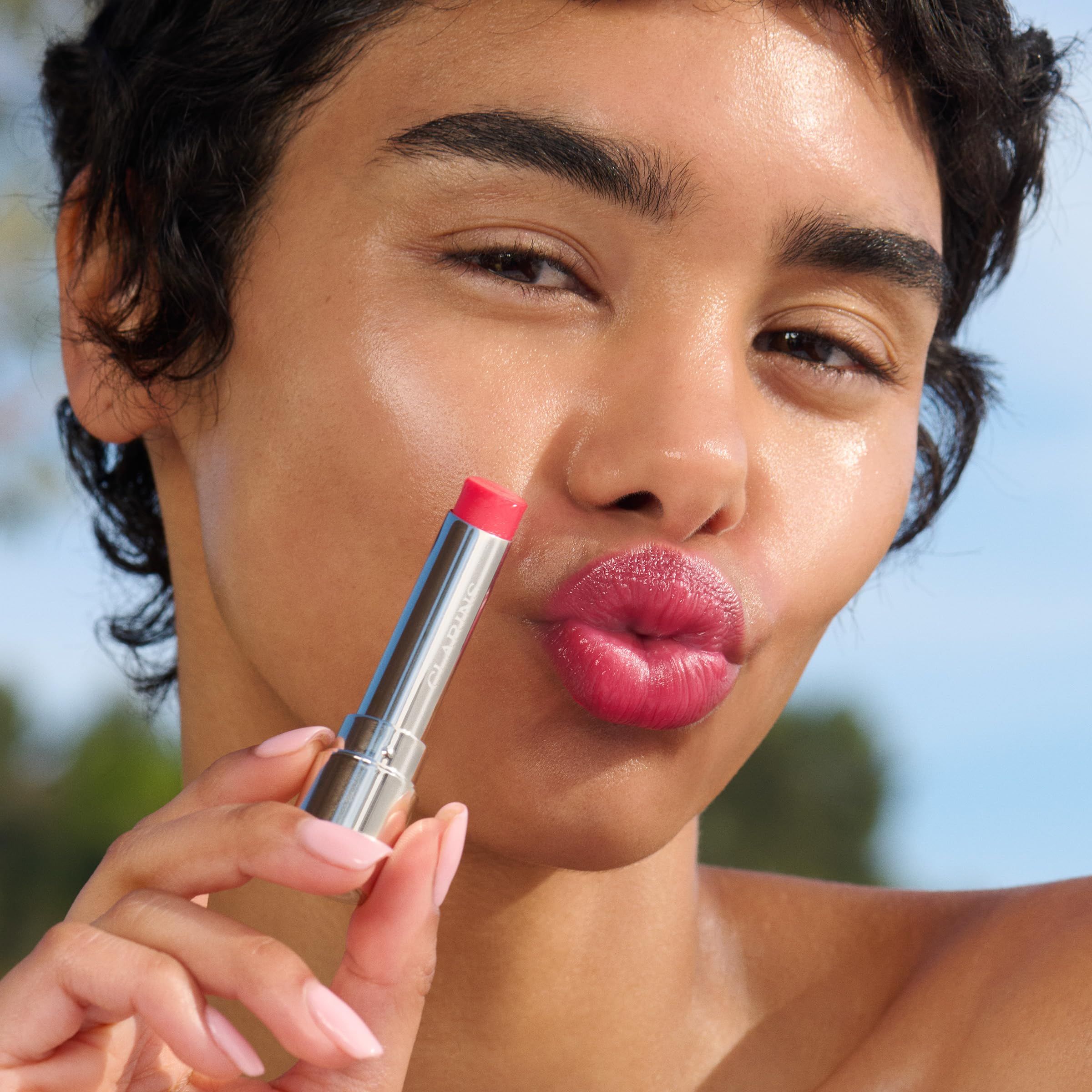 Eine Frau hält einen Lippenbalsam. Die Lippen sind mit dem Produkt bedeckt. Hintergrund: blauer Himmel.