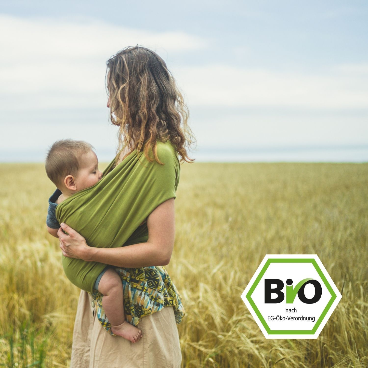 Frau mit Baby im Tragetuch auf einem Feld. Bio-Siegel im Vordergrund.
