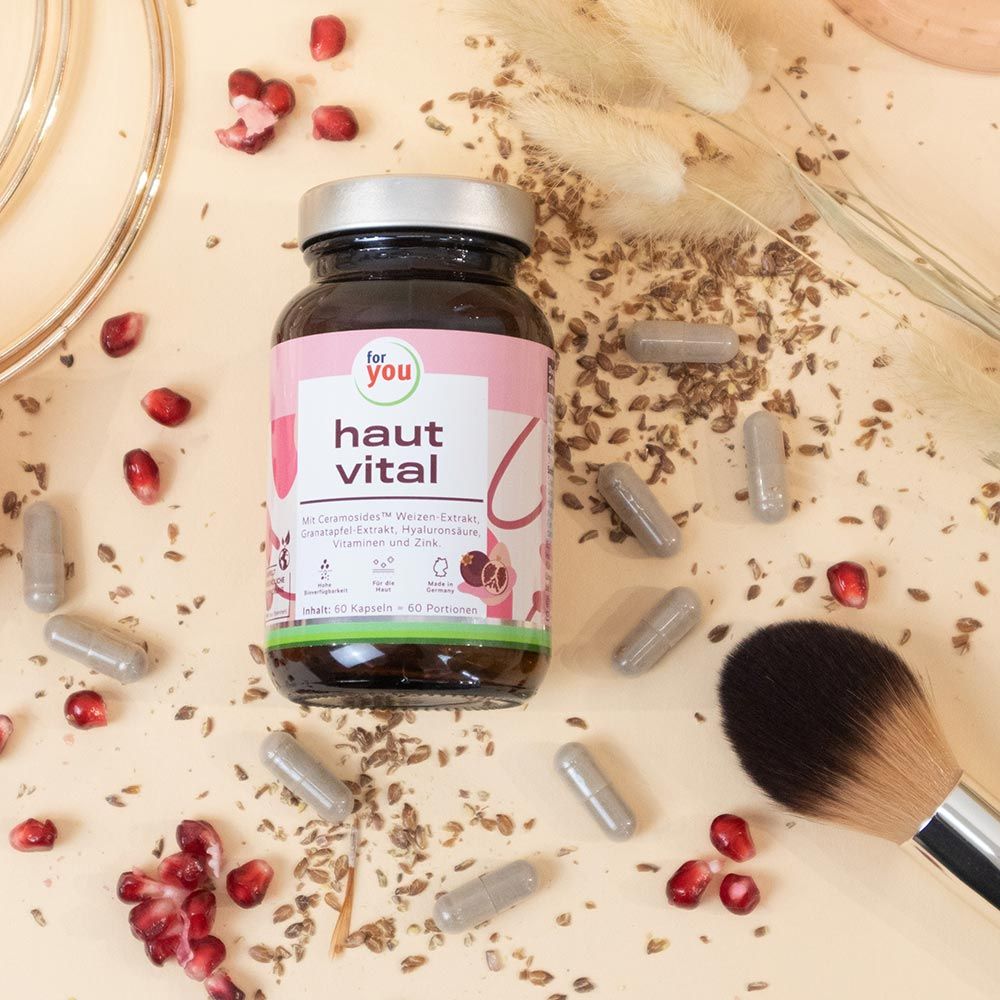 Flasche mit rosa Etikett, Aufschrift: for you haut vital. Kapseln und Granatapfelkerne liegen verstreut. Pinsel.