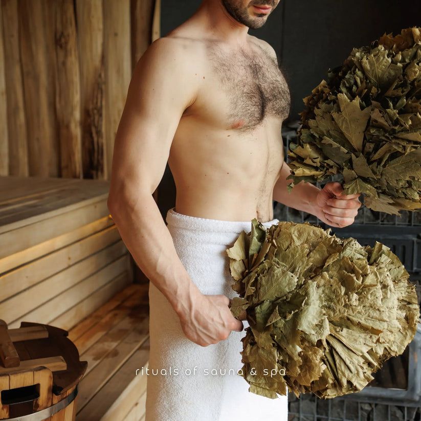 Mann hält zwei Bündel Blätter. Im Hintergrund Sauna-Elemente.