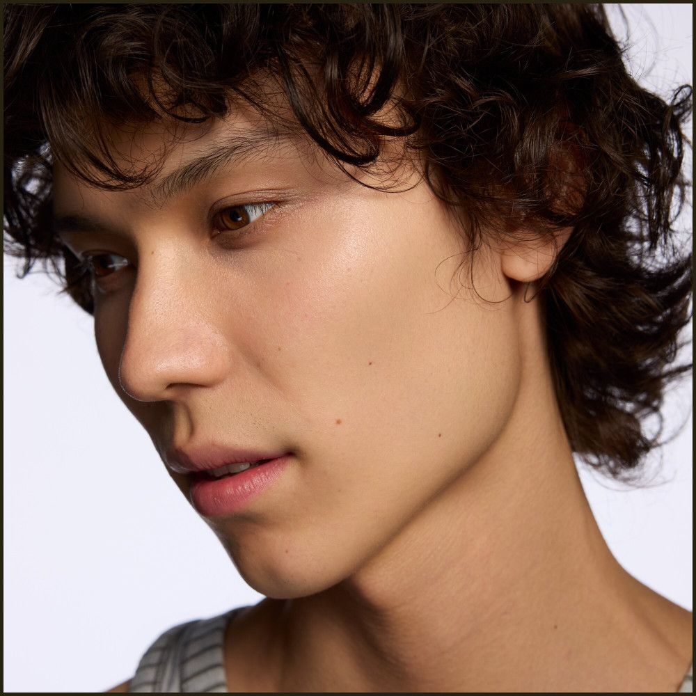 Nahaufnahme eines Mannes mit lockigem Haar. Er blickt nach unten. Hautton ist hell.