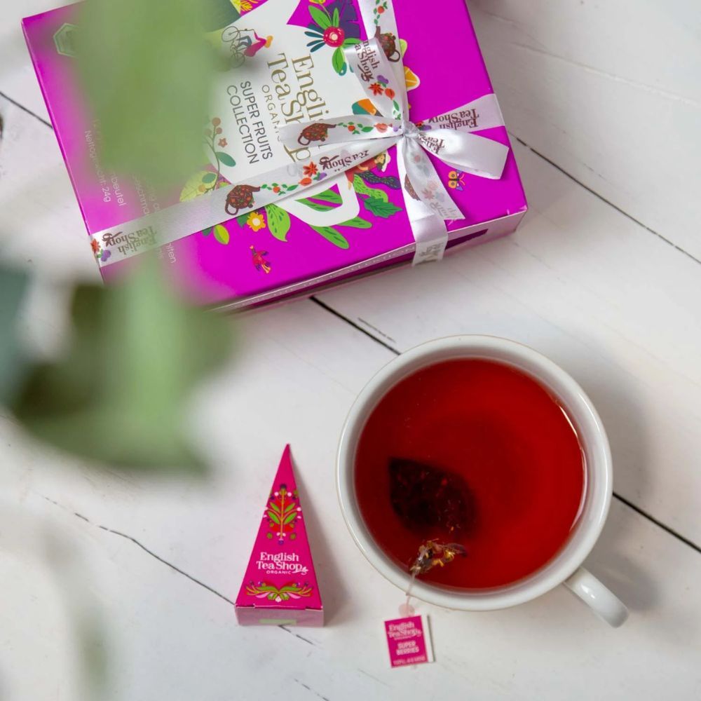 Tasse Tee mit Pyramiden-Teebeutel und Teebeutel-Etikett. Rosa Pyramiden-Teebeutel daneben. Aufschrift: English Tea Shop.