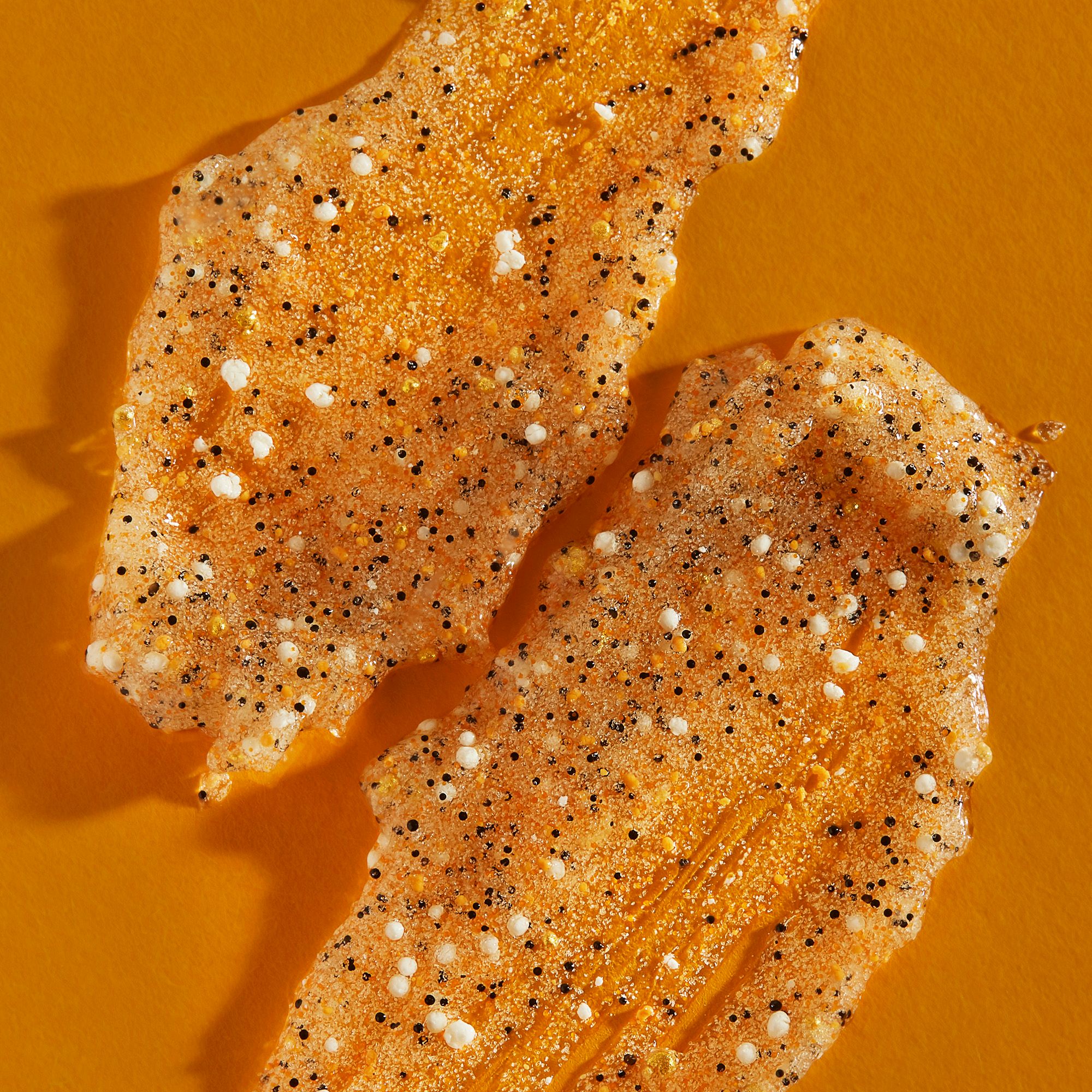 Zwei orangefarbene Peeling-Stücke mit weißen und schwarzen Partikeln. Auf orangefarbenem Hintergrund.