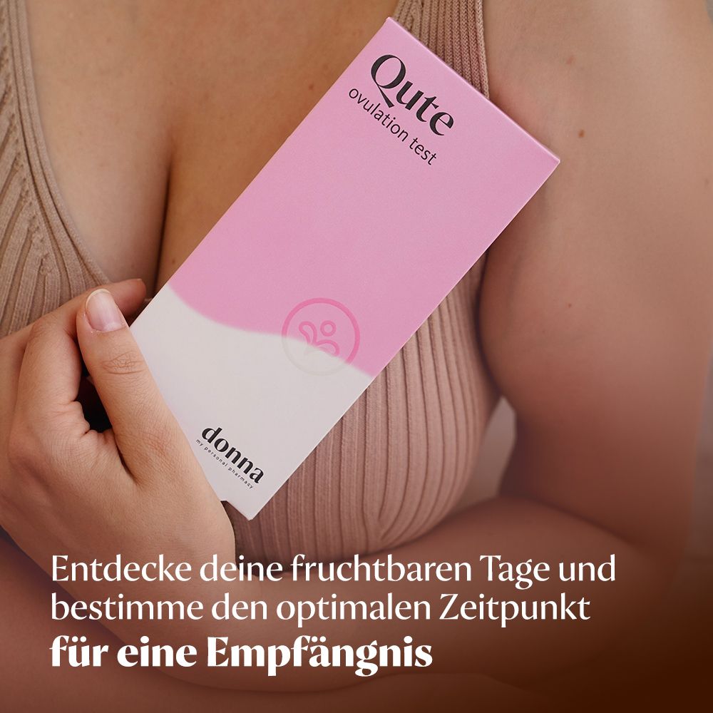 Eine Frau hält eine Qute Ovulationstest-Packung. Aufschrift: Qute Ovulationstest. Rosa Verpackung mit weißem Text.