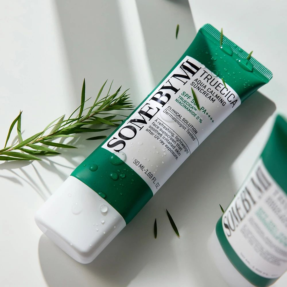 Grüne und weiße Tube mit Sonnencreme. Text: SOMEBYMI, TRUECICA Aqua Calming Suncream, SPF 50+ PA++++. Wasser und Blätter.