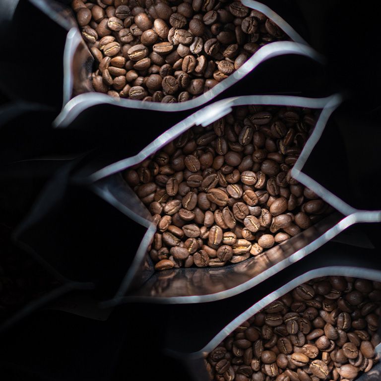 Drei offene Packungen mit gerösteten Kaffeebohnen.