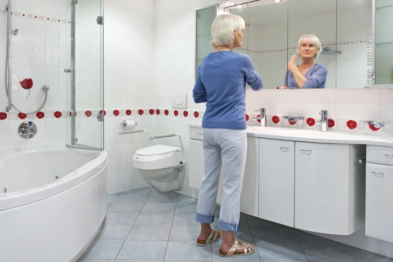 Frau im Badezimmer vor Spiegel. Toilettensitzerhöhung mit Armlehnen.