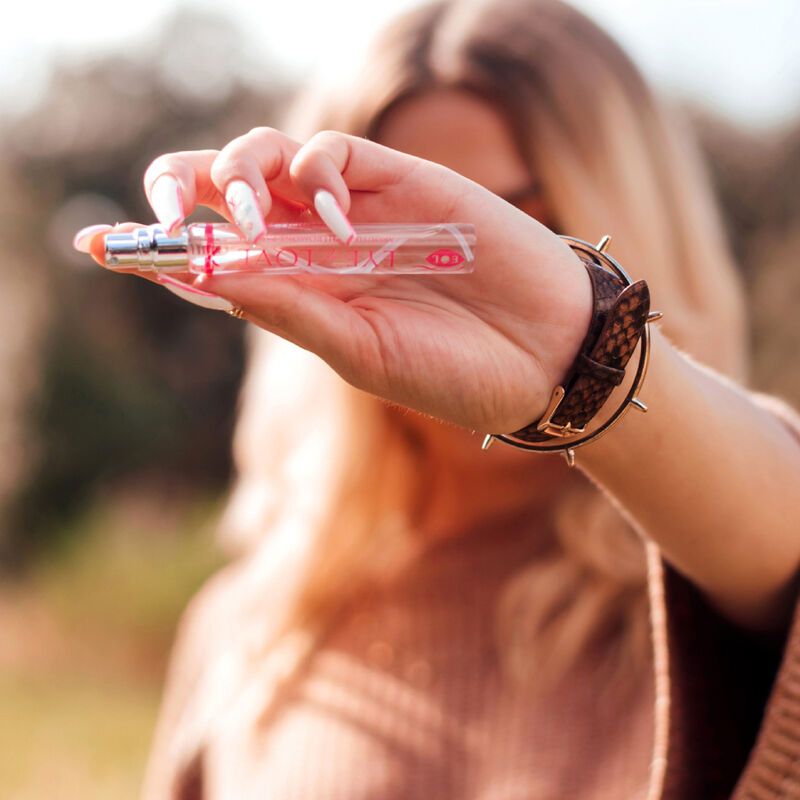 Parfumflakon in Hand gehalten. Aufschrift: EYE OF LOVE PHEROMONE PARFUM. Flakon mit Sprühkopf. Frau mit Armband.