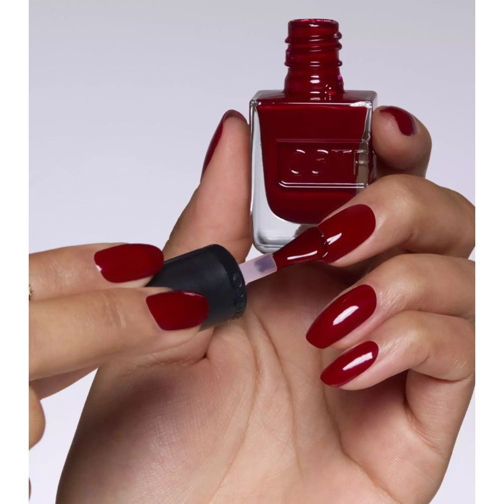 Hand mit lackierten Nägeln. Roter Nagellack. Nagellackflasche mit Pinsel. Schwarzer Deckel. "catrice" Schriftzug.