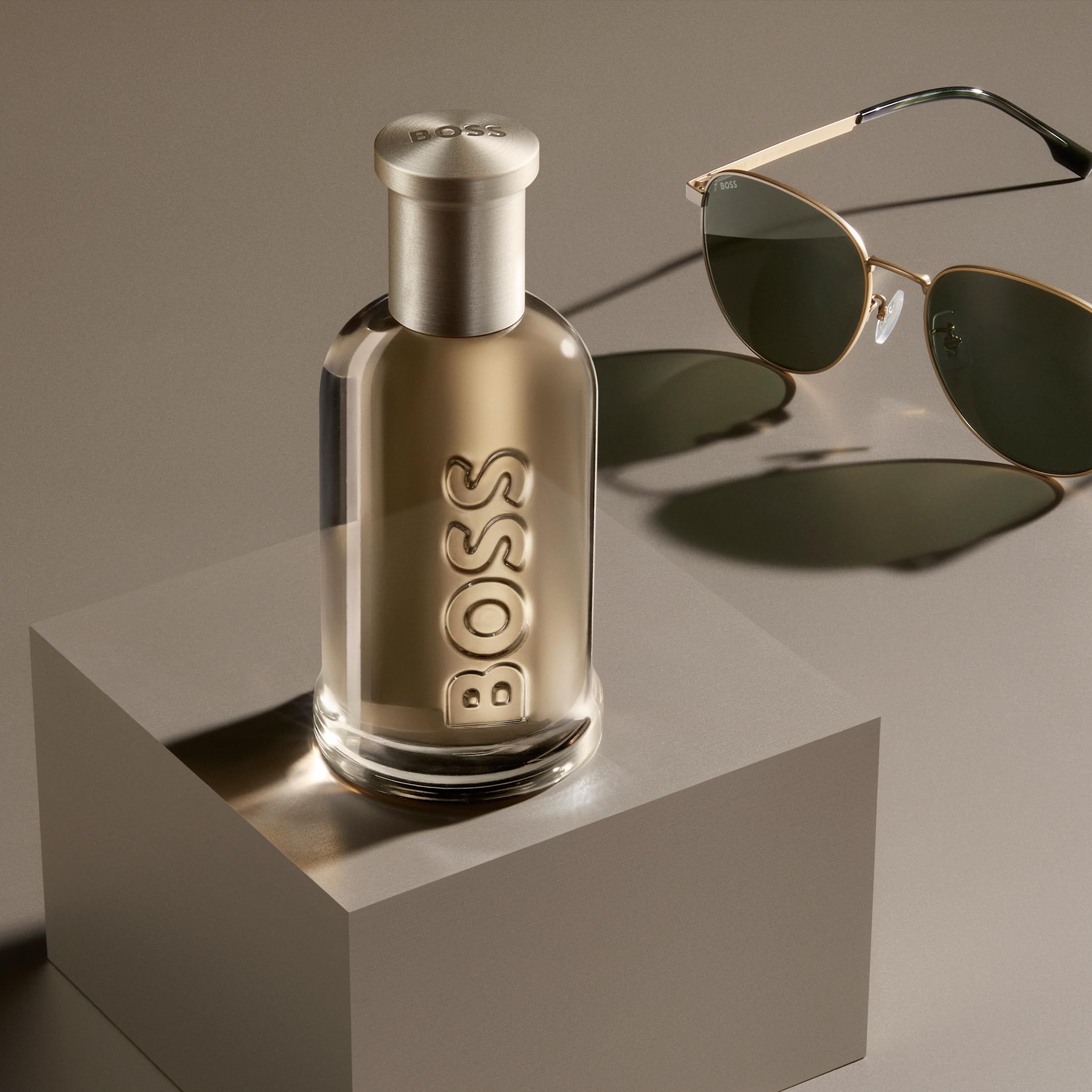 Hugo Boss Bottled Eau de Parfum Flakon auf einem Würfel, neben Sonnenbrille.