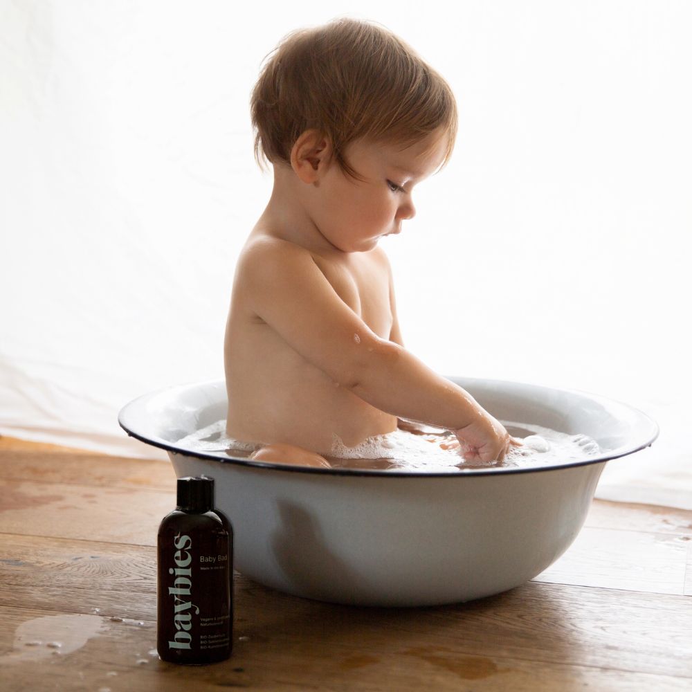 Baby sitzt in einer Schüssel mit Wasser, daneben steht eine Flasche Baybies Baby Bad.