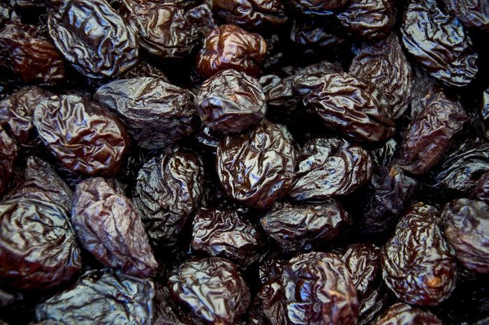 Nahaufnahme von vielen dunklen, getrockneten Pflaumen. Die Früchte haben eine runzlige Oberfläche.