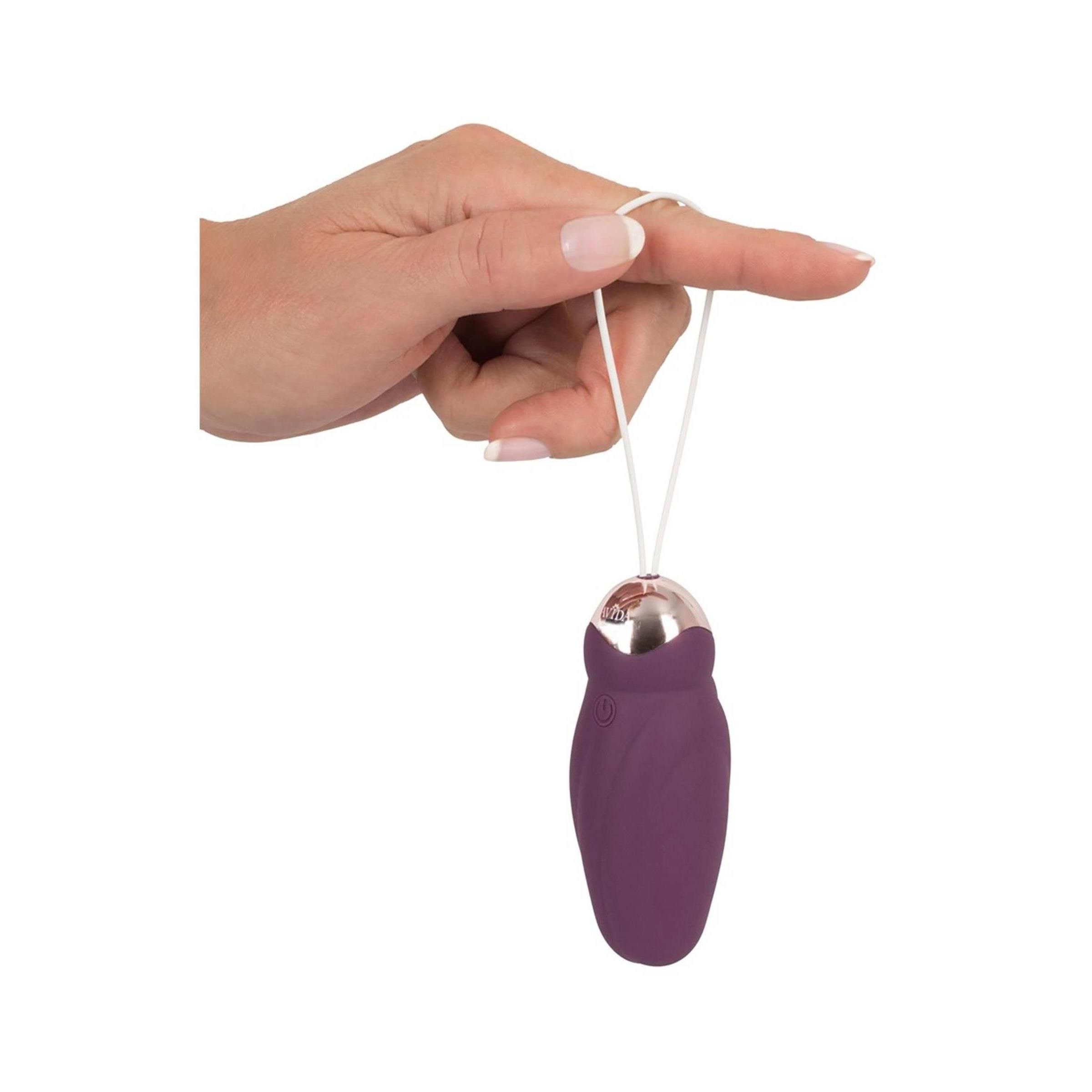 Finger hält Schlaufe der Vibrationskugel. Kugel in Lila und Gold. Hintergrund weiß.
