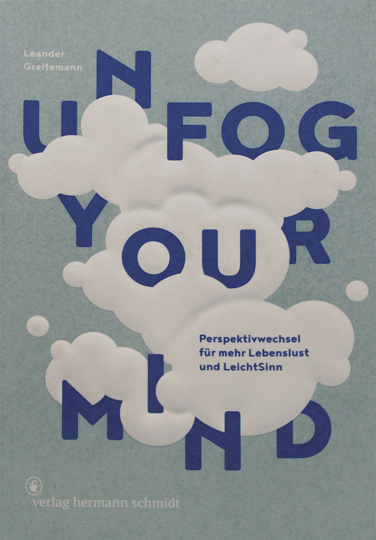 Buchcover mit Titel "Unfog your mind". Blaue Schrift auf hellblauem Hintergrund. Wolken-Illustrationen. Autor: Leander Greitemann.