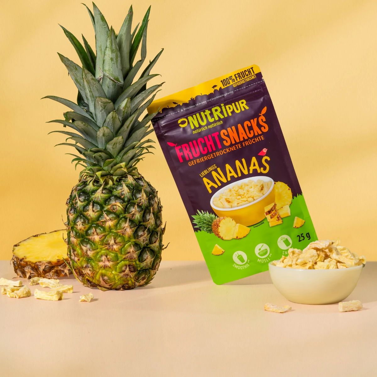 Beutel mit gefriergetrockneten Ananas-Bits, daneben eine Ananas und eine Schale mit Ananas-Bits. Aufschrift: NutriPur, Fruchtsnacks.