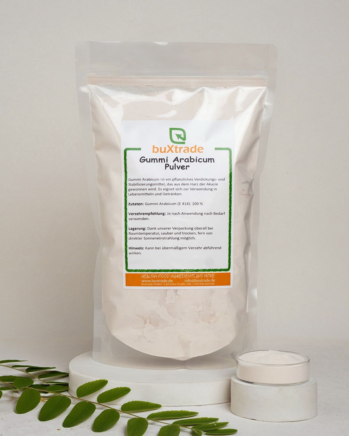 Buxtrade Gummi Arabicum Pulver in einem Beutel, daneben eine kleine Dose und Blätter.