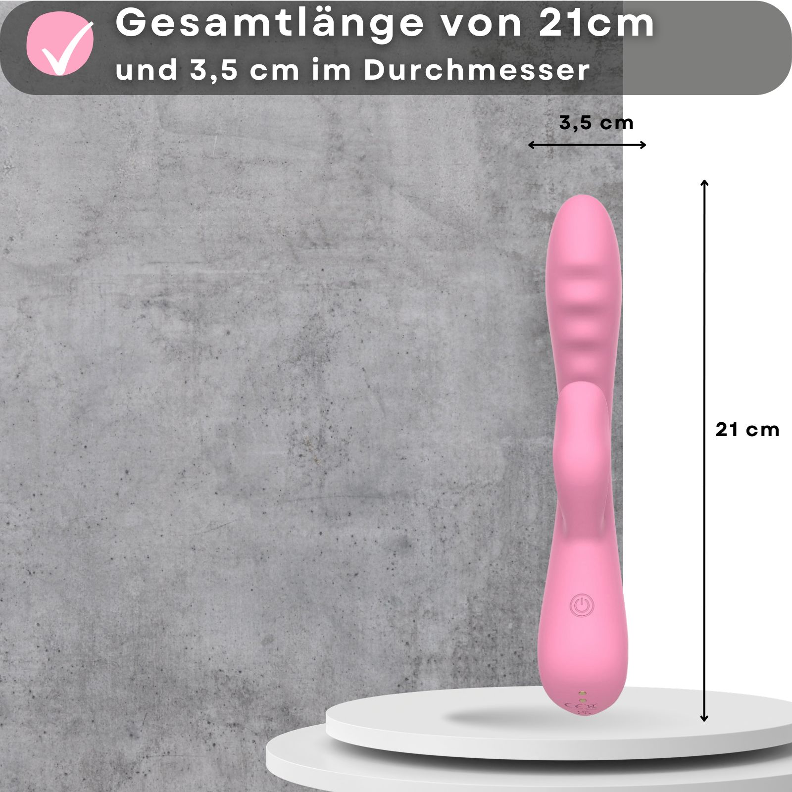 Rosa Vibrator. 21cm lang, 3,5cm Durchmesser. Auf Podest. USB-aufladbar. 10 Vibrationsmodi. Hintergrund: Hände.