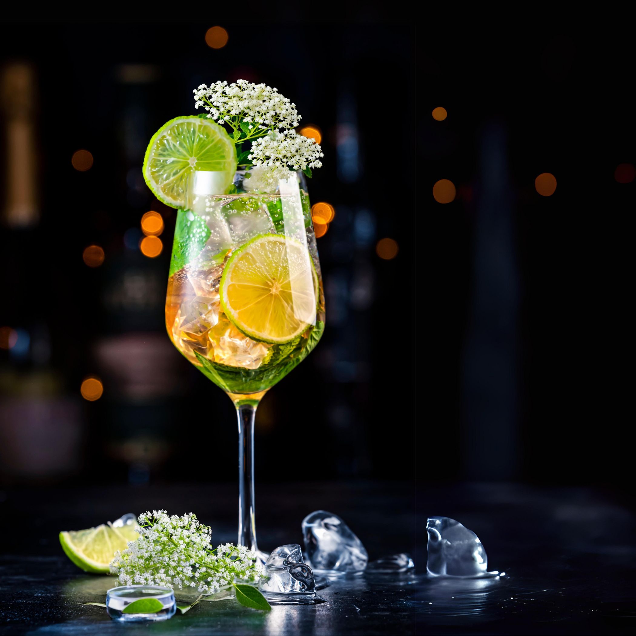 Glas mit Getränk, Eiswürfeln, Limettenscheiben und Blüten. Dunkler Hintergrund. Dekoration mit Blüten und Limettenscheiben.