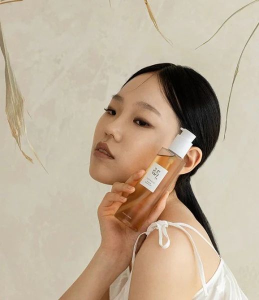 Eine Frau hält eine Flasche Beauty of Joseon Revive Serum an ihre Wange.