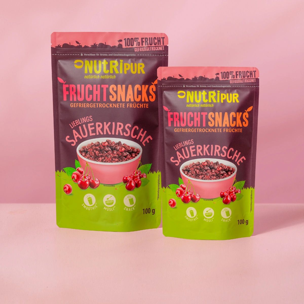 Zwei Beutel mit gefriergetrockneten Sauerkirschen. Aufschrift: NutriPur, Frucht Snacks, Sauerkirsche, 100g. Rosa Hintergrund.